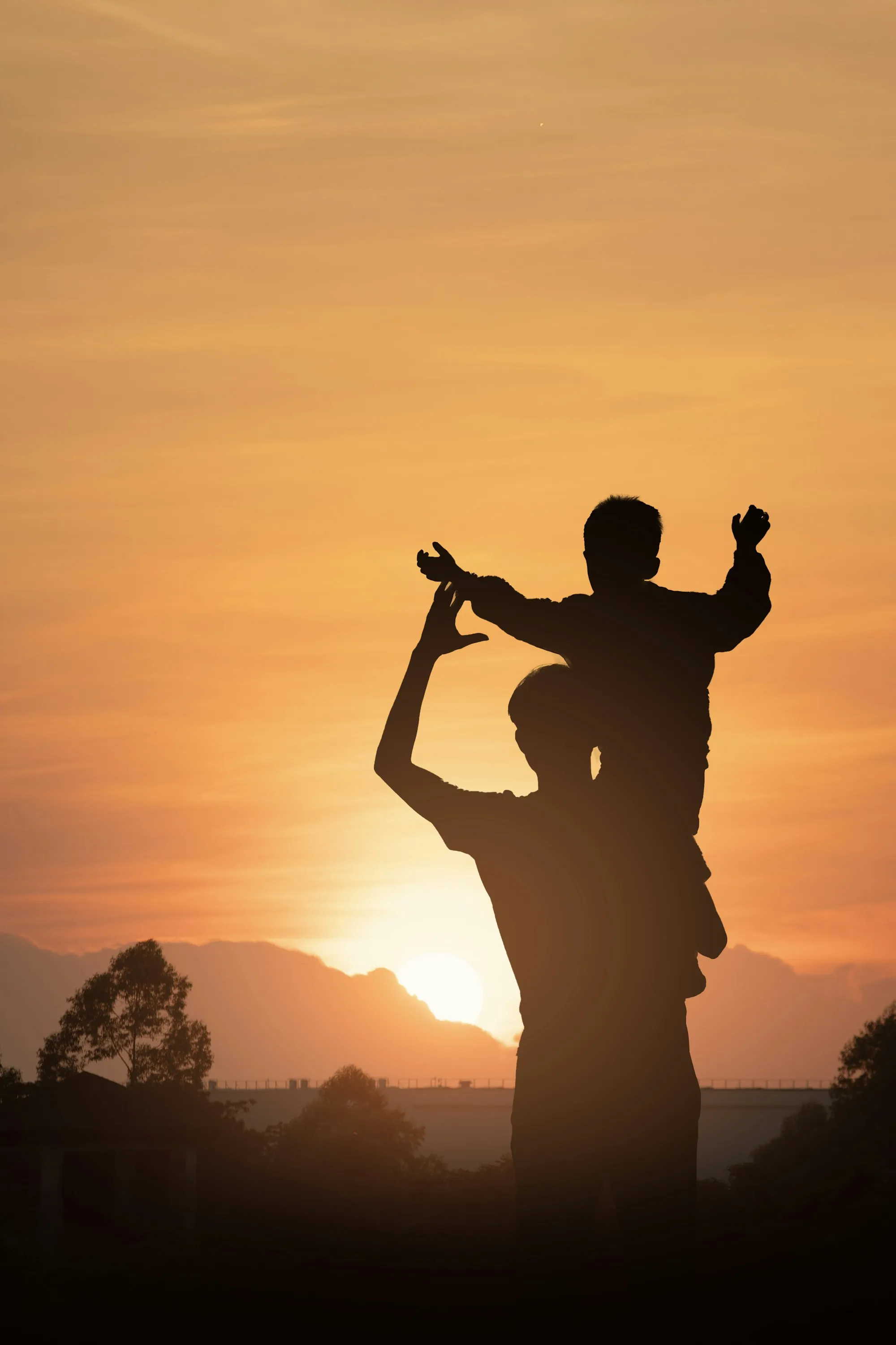 Silhouette of a child riding on a parent's shoulders at sunset