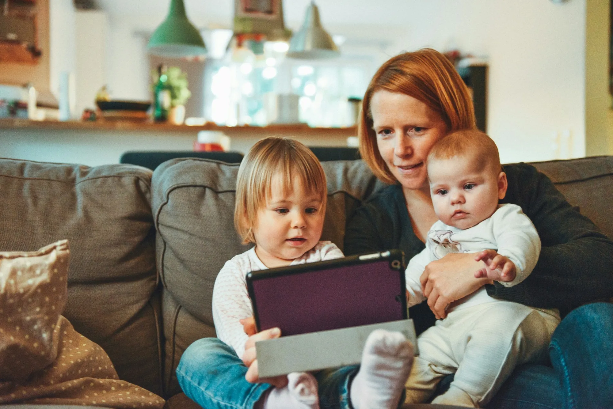 Mother on the couch reading a tablet with two small children