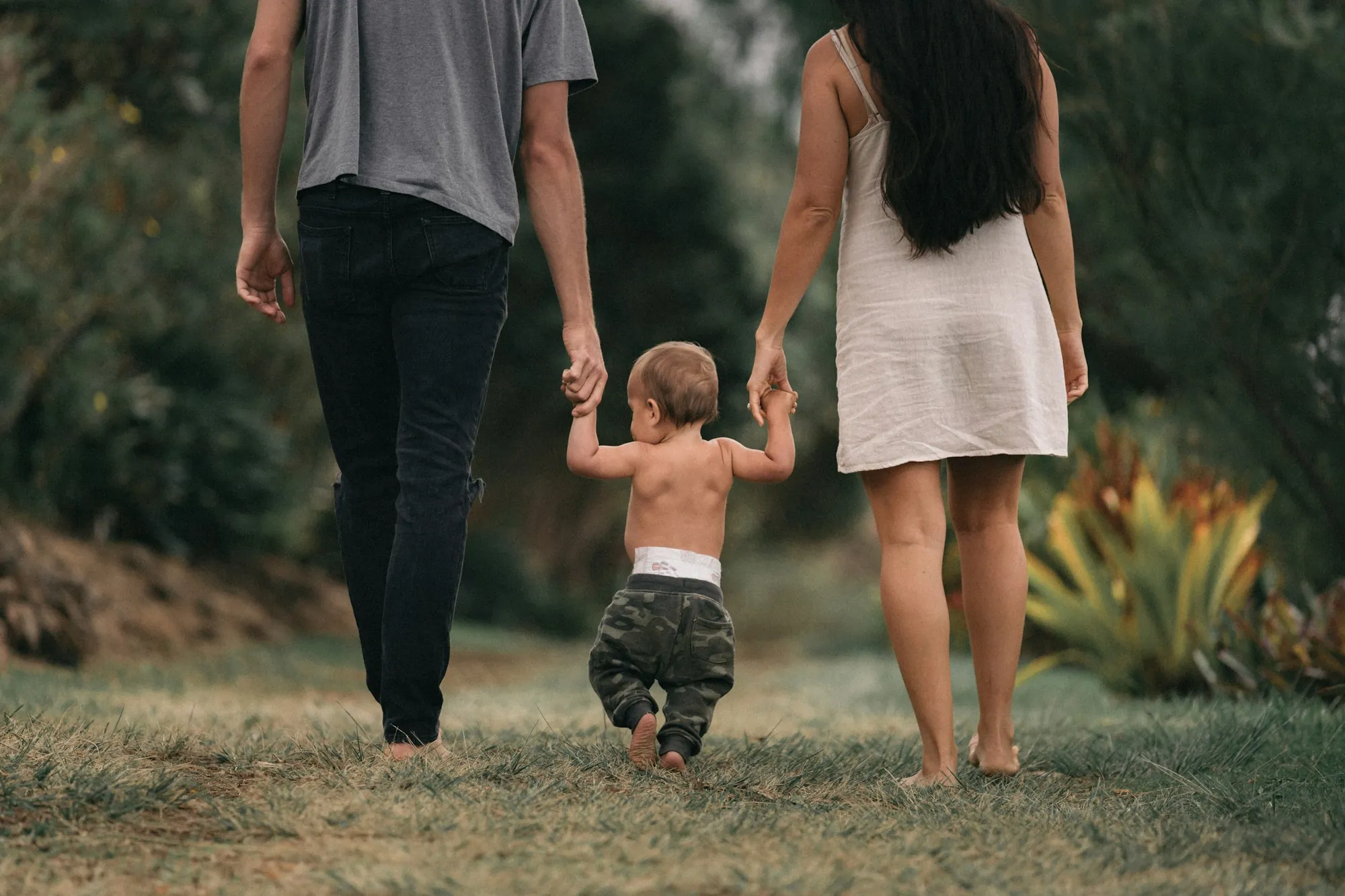 Parents holding a toddler's hands as he walks between them on the grass, weighing term vs whole life insurance for young parents in Riverwoods